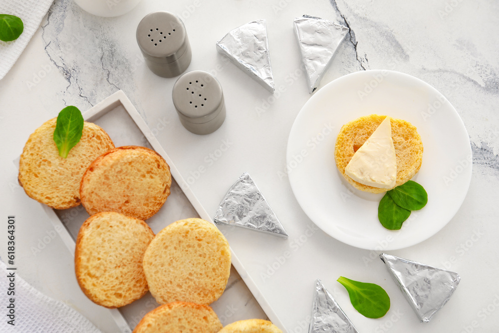 Plates with croutons and triangles of tasty processed cheese on white marble background