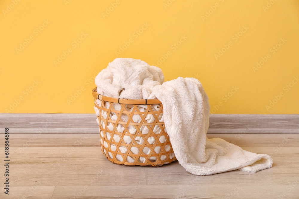 Basket with new soft blanket near yellow wall in room