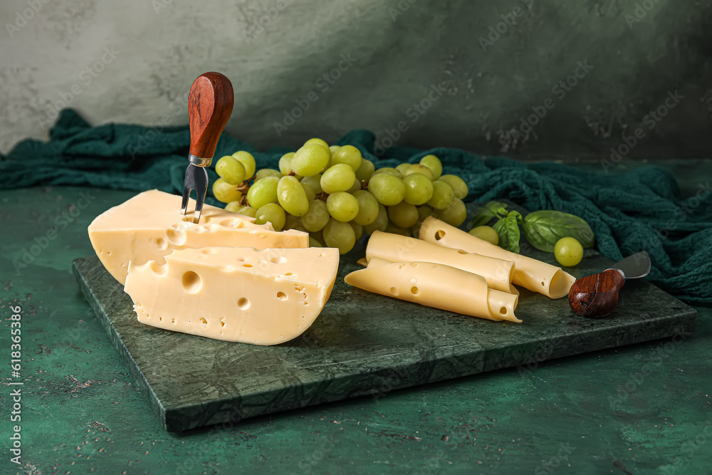 Board with tasty Swiss cheese and grapes on table