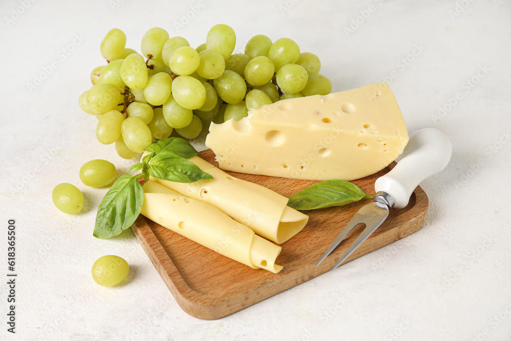 Wooden board with tasty Swiss cheese and grapes on light background