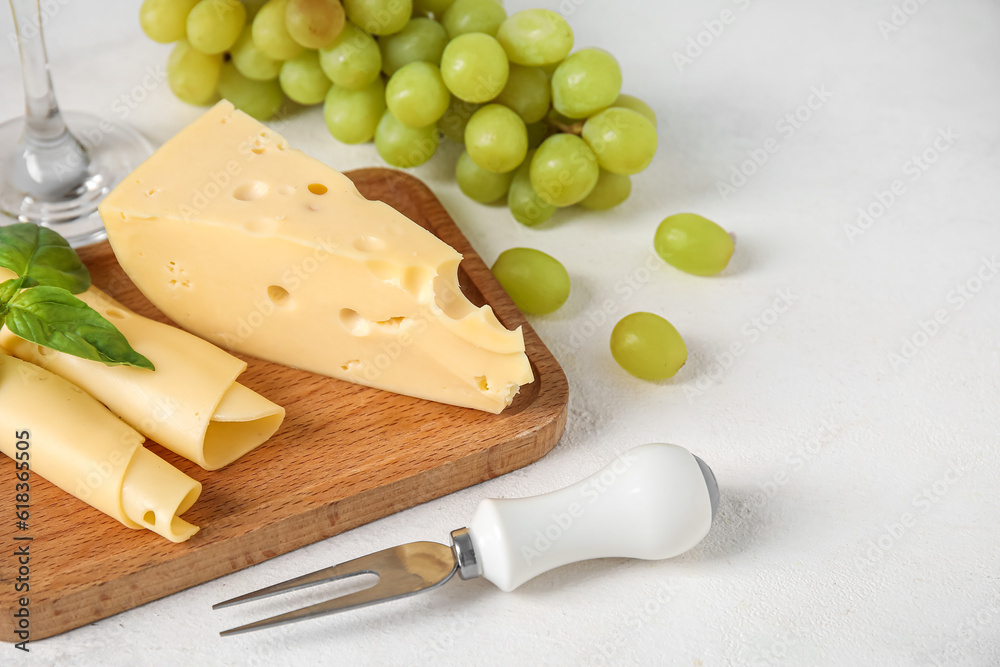 Wooden board with tasty Swiss cheese and grapes on light background