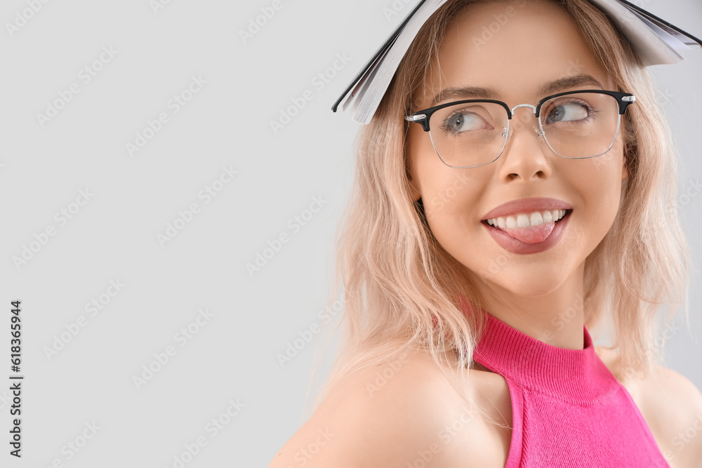 Young woman in stylish eyeglasses with book on light background, closeup