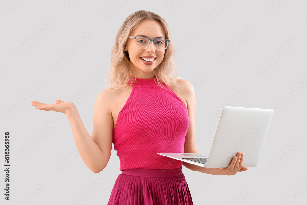 Young woman in stylish eyeglasses with laptop on light background