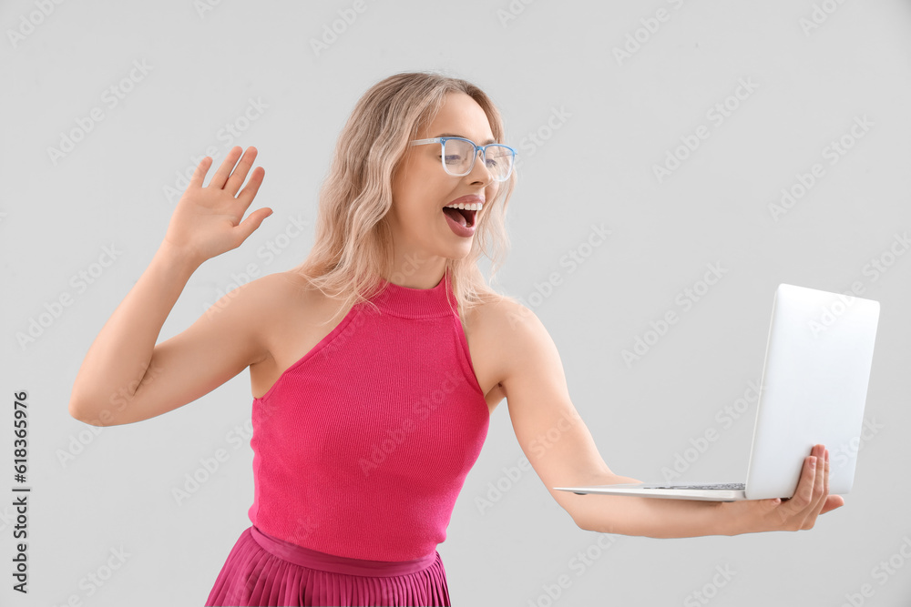 Young woman in stylish eyeglasses with laptop on light background