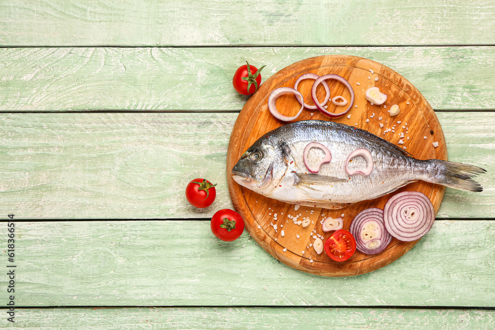 Board of raw dorado fish with vegetables on green wooden background