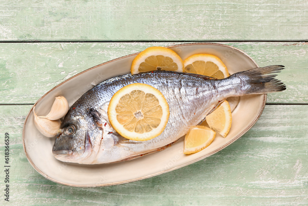 Plate of raw dorado fish with lemon on green wooden background