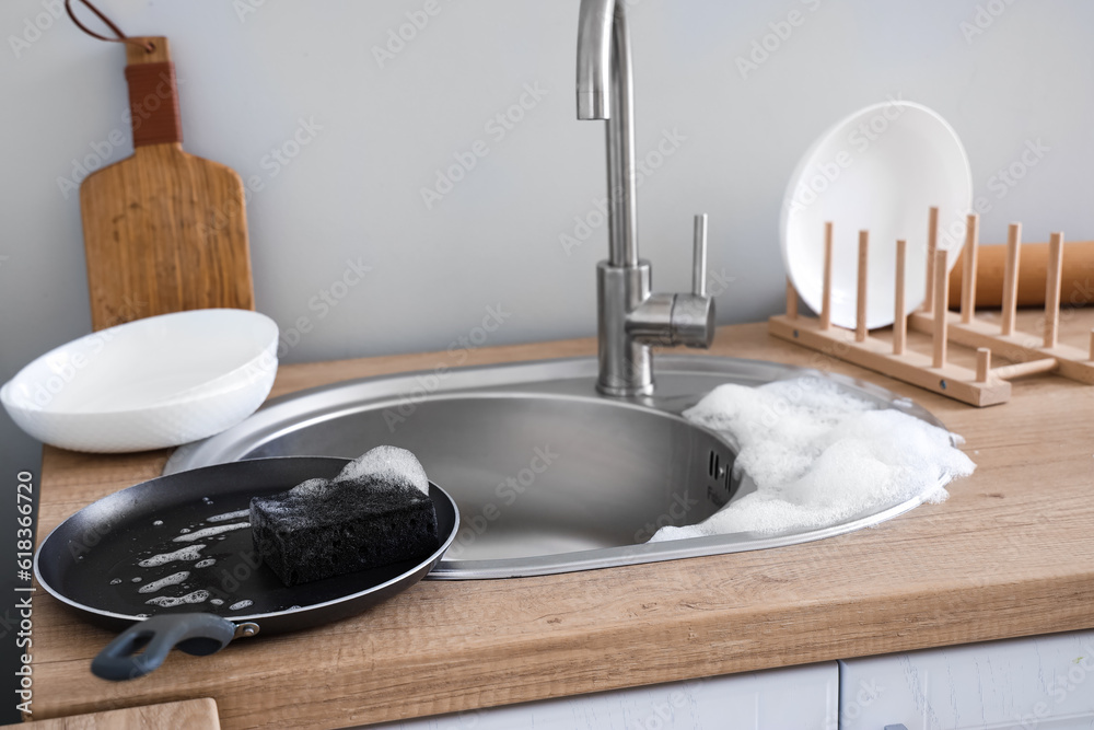 Frying pan with foam and sponge on countertop near sink in kitchen