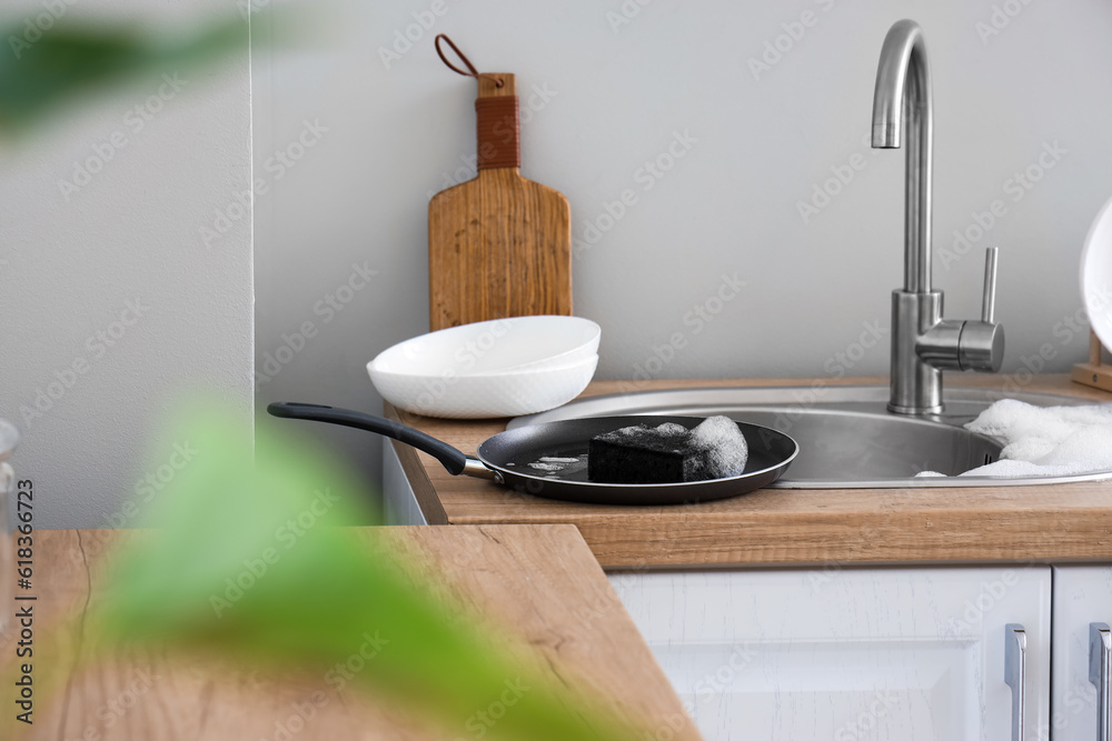 Frying pan with foam and sponge on countertop near sink in kitchen