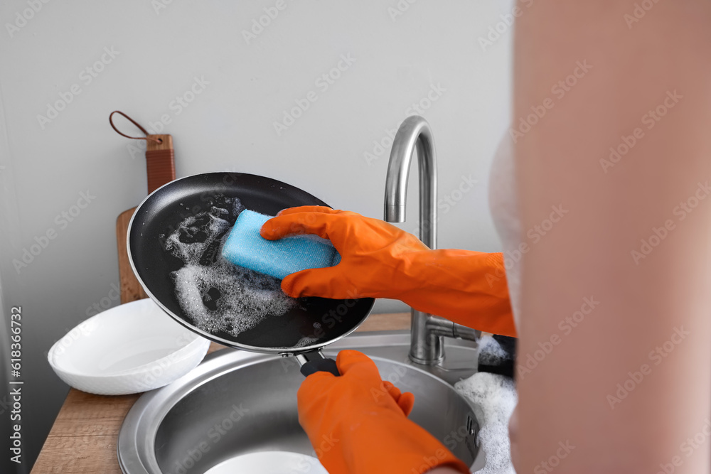 Woman in orange rubber gloves cleaning washing frying pan with sponge