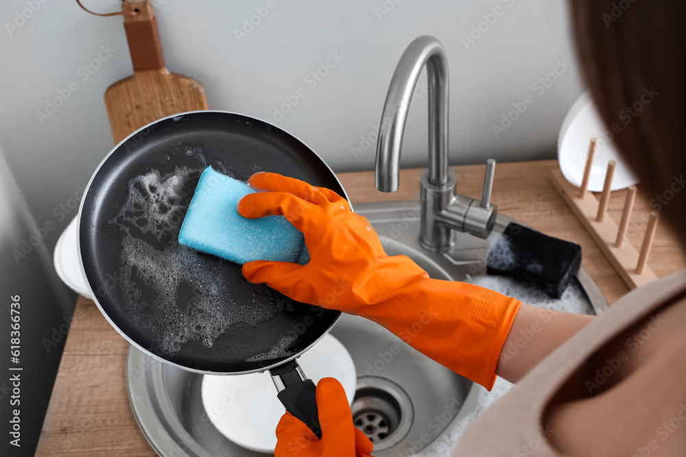 Woman in orange rubber gloves cleaning washing frying pan with sponge