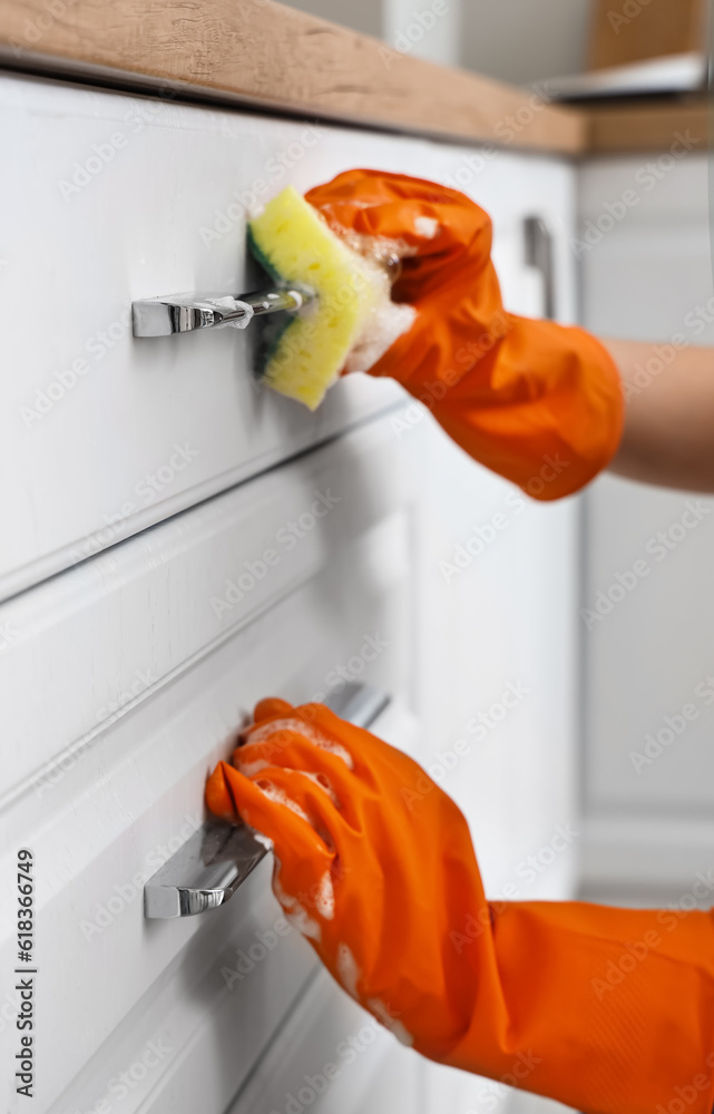 Woman in orange rubber gloves cleaning drawers of kitchen counter with sponge