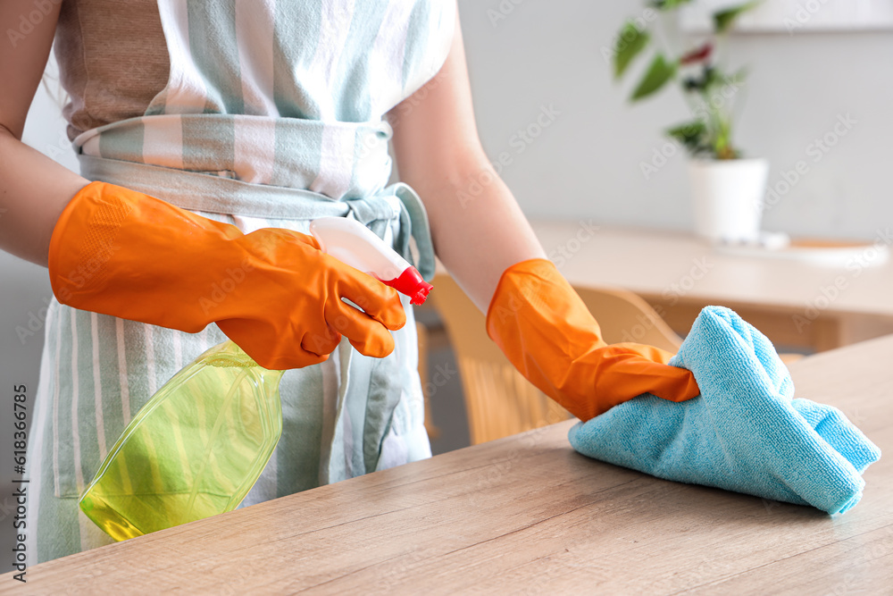 Woman in orange rubber gloves cleaning wooden countertop with rag and detergent