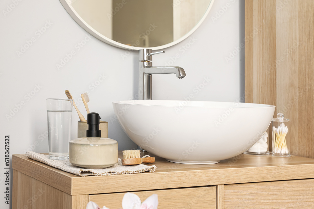 Sink bowl and bath accessories on wooden cabinet in bathroom