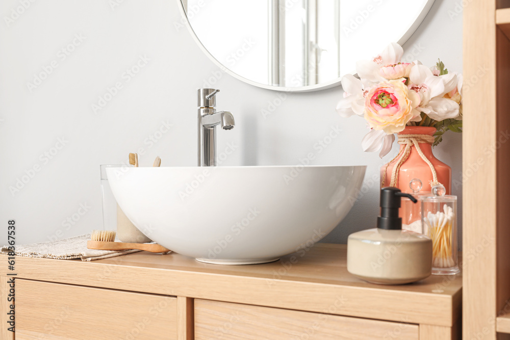 Sink bowl and bath accessories on wooden cabinet in bathroom