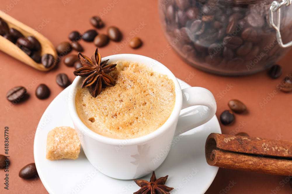 Cup of hot espresso and jar with coffee beans on brown background