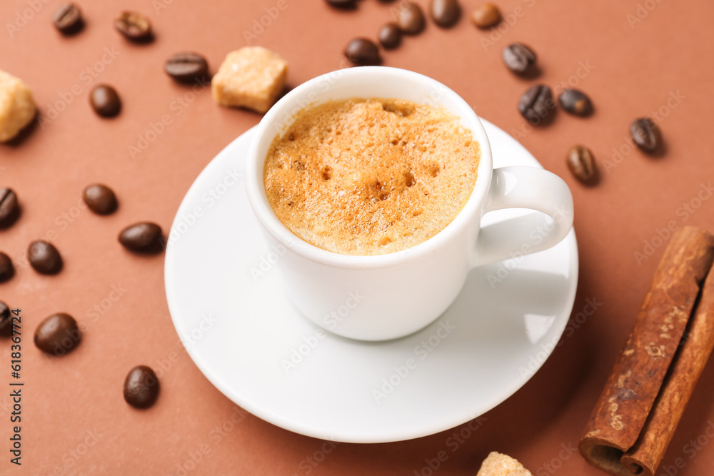 Cup of hot espresso and coffee beans on brown background