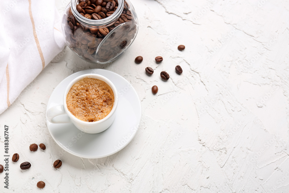 Cup of hot espresso and jar with coffee beans on white background