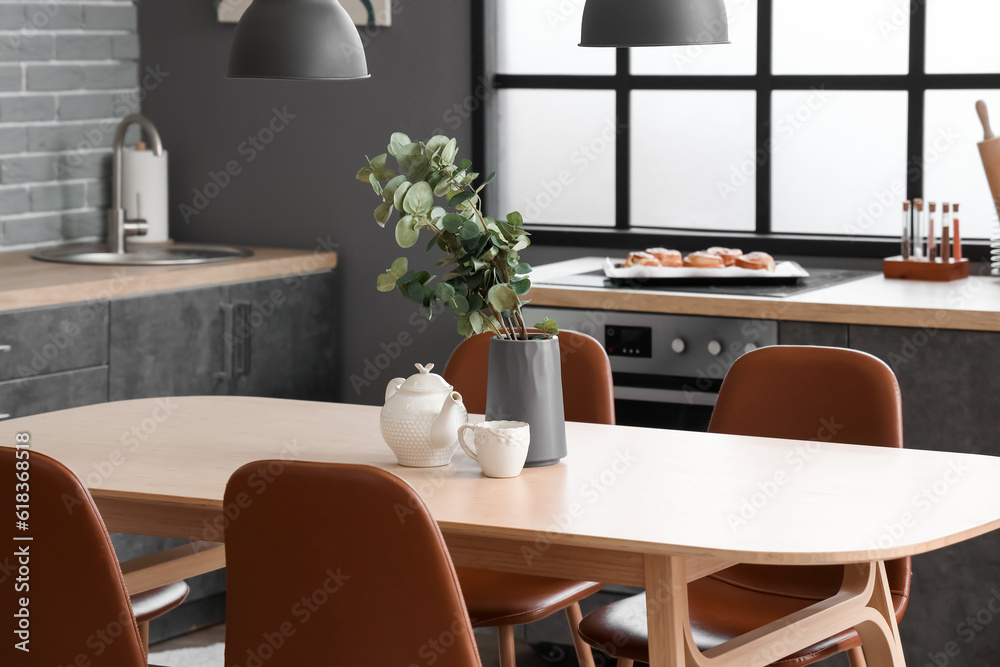 Wooden dining table with teapot, cup and eucalyptus branches in interior of modern kitchen