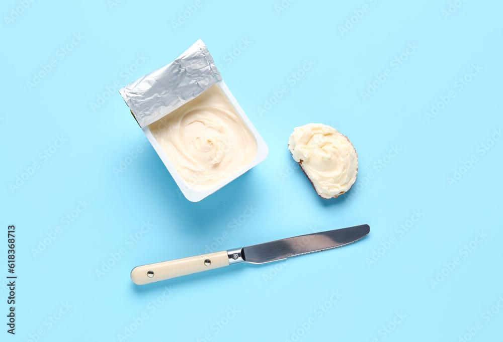 Plastic container and sandwich with tasty cream cheese on blue background