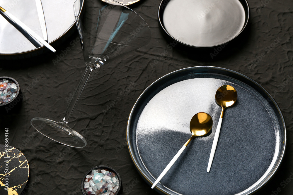 Clean plate, spoons and glass on black table