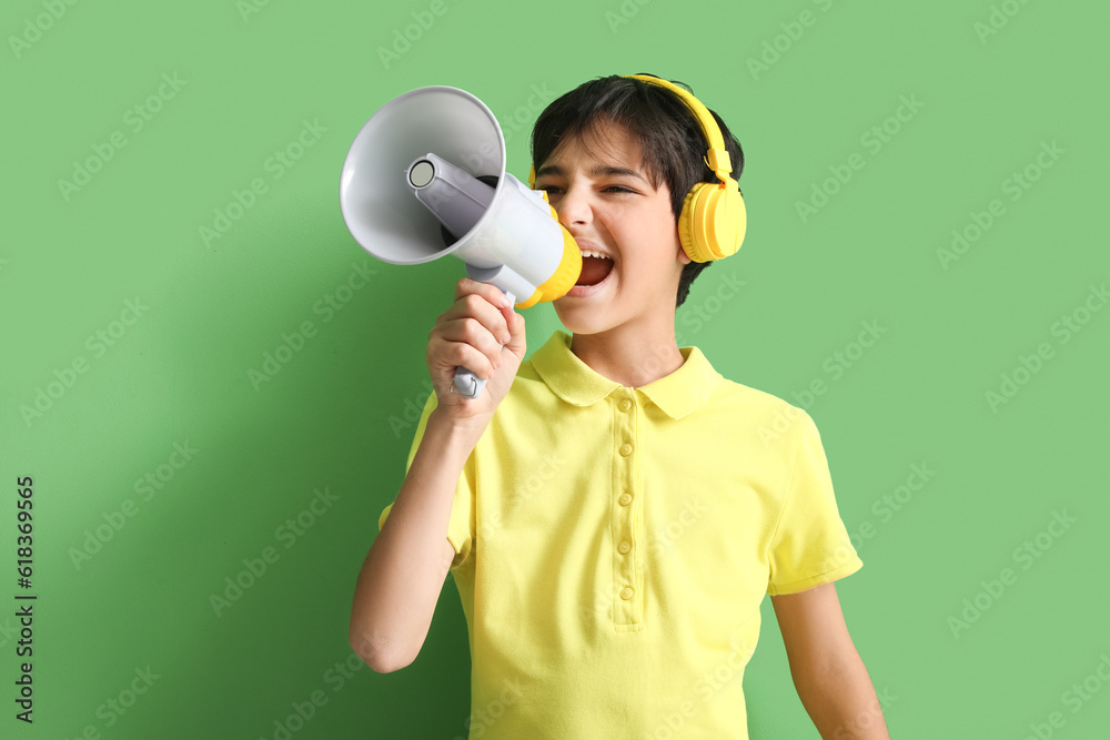 Little boy with headphones shouting into megaphone on green background