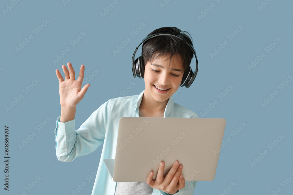 Little boy in headphones with laptop video chatting on blue background