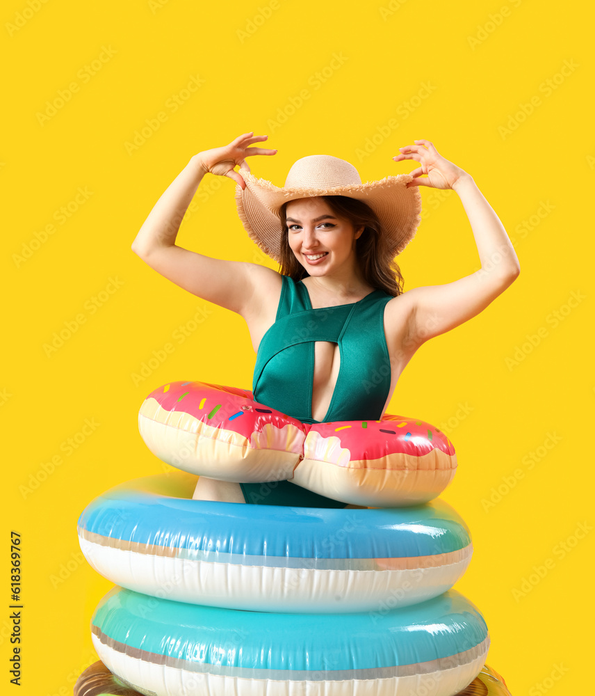 Young woman with swim rings on yellow background