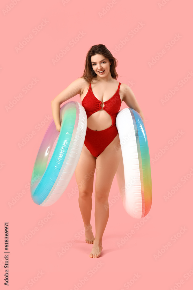 Young woman with swim rings on pink background