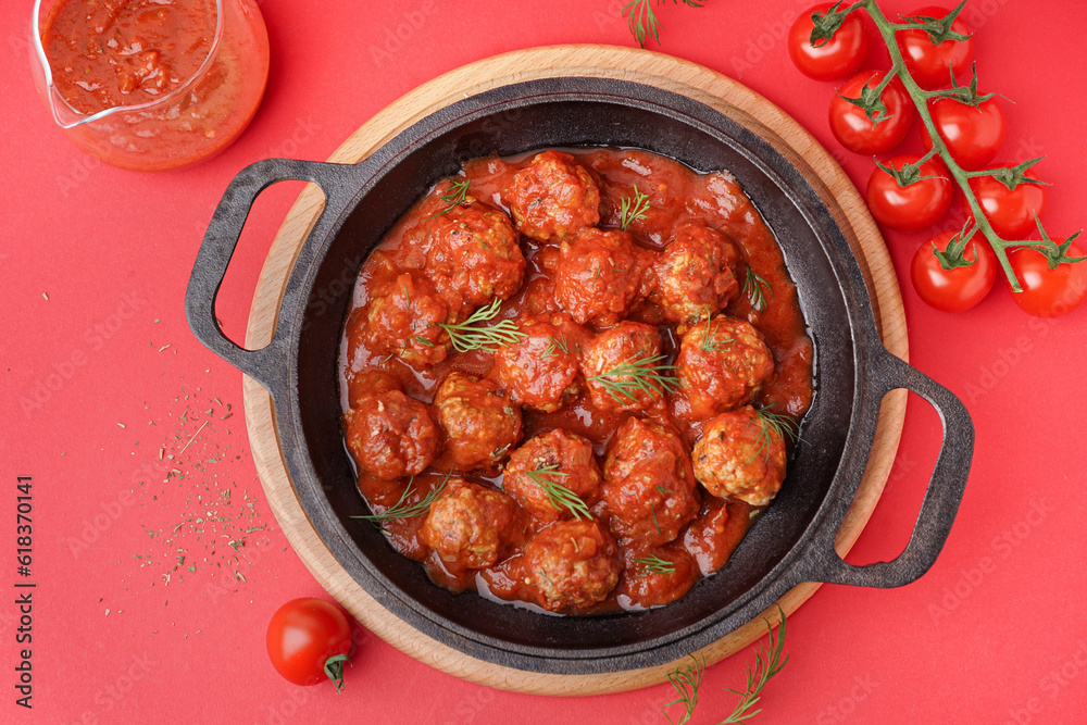 Frying pan of tasty meat balls with tomato sauce and dill on red background