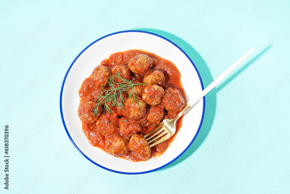 Bowl of tasty meat balls with tomato sauce and dill on blue background