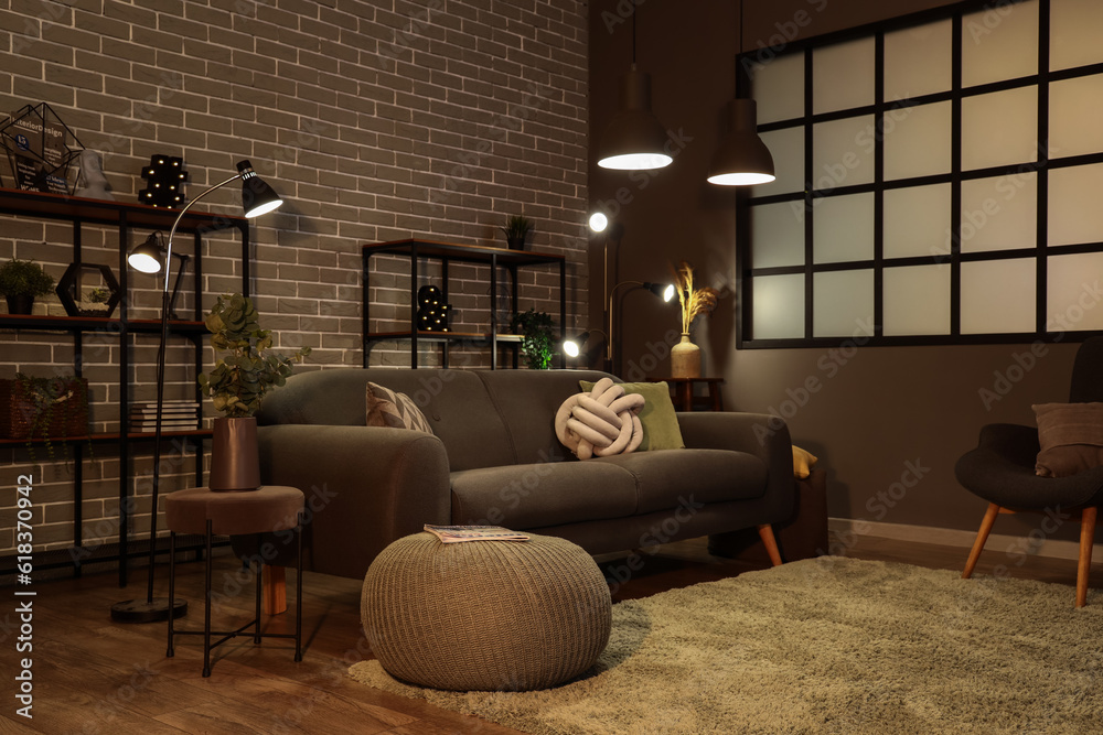 Interior of dark living room with cozy grey sofa and glowing lamps