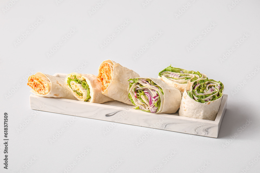 Plate of tasty lavash rolls with vegetables on grey background