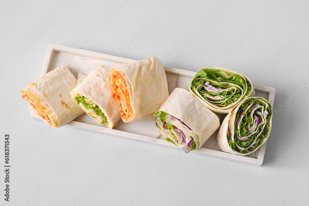 Plate of tasty lavash rolls with vegetables on grey background