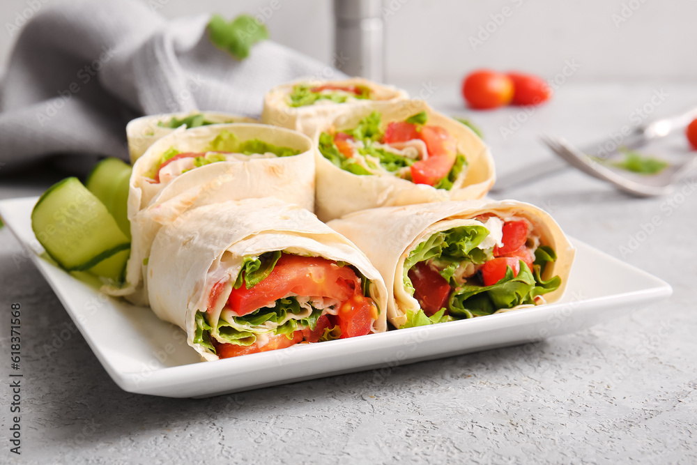 Plate of tasty lavash rolls with vegetables on grey background