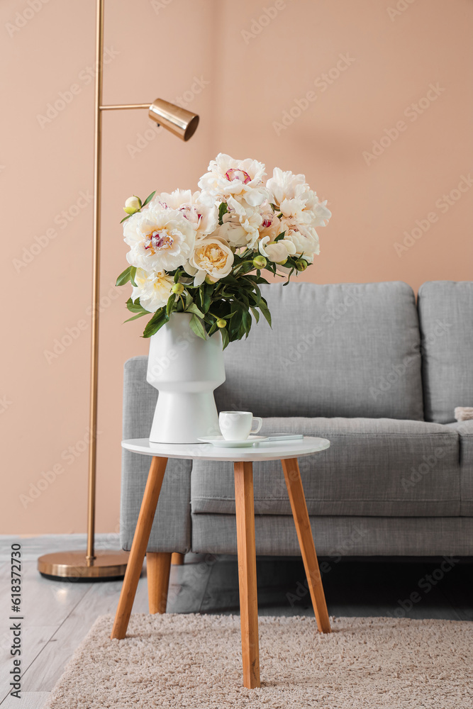 Vase of white peonies with coffee table, couch and floor lamp near beige wall