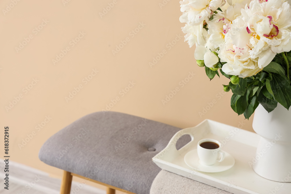 Vase of white peonies with cup of coffee on tray near beige wall