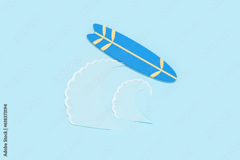 Creative composition with mini surfboard and paper waves on blue background