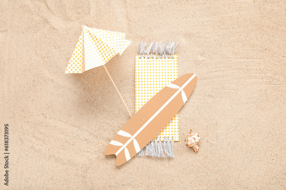 Creative composition with mini surfboard, umbrella and blanket on sand