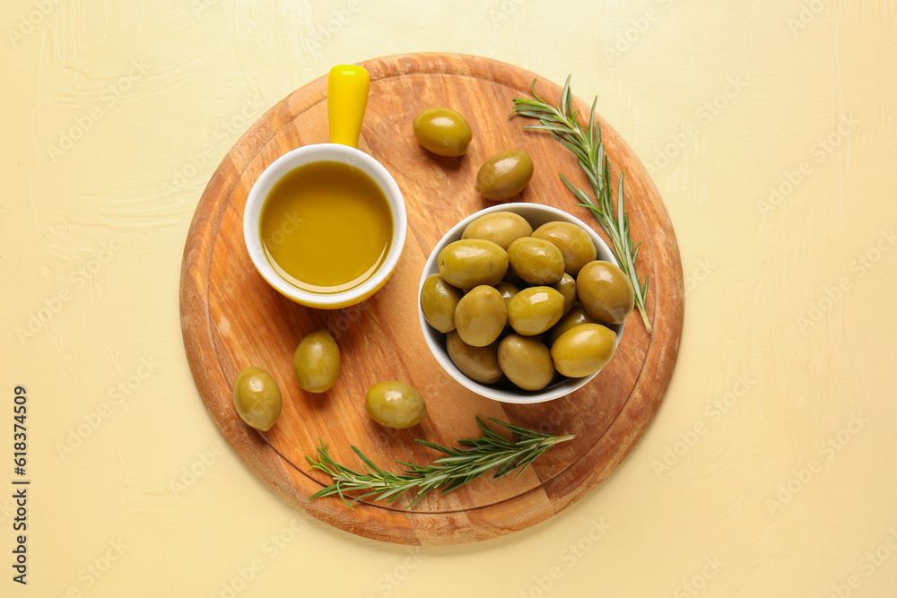 Bowls with ripe olives and oil on yellow background