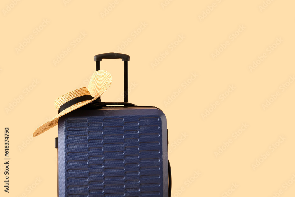 Suitcase with wicker hat on pale orange background. Travel concept