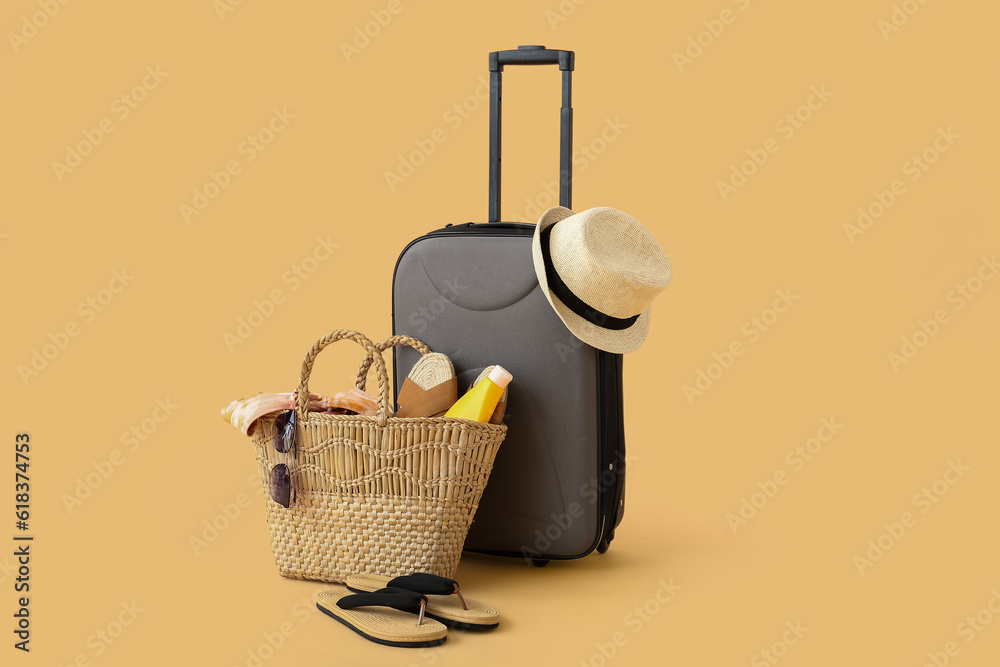 Suitcase with wicker hat, bag and beach accessories on beige background. Travel concept