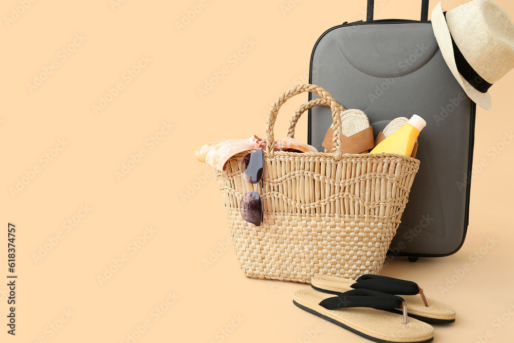 Suitcase with wicker hat, bag and beach accessories on pale orange background. Travel concept