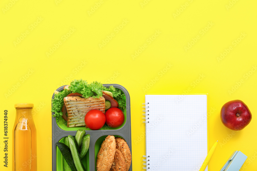 Stationery, blank notebook, drink and lunch box with tasty food on yellow background