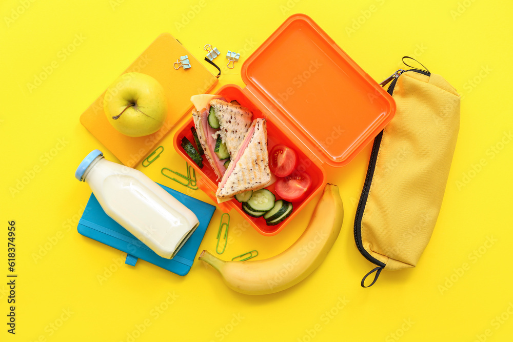 Different stationery, drink and lunch box with tasty food on yellow background