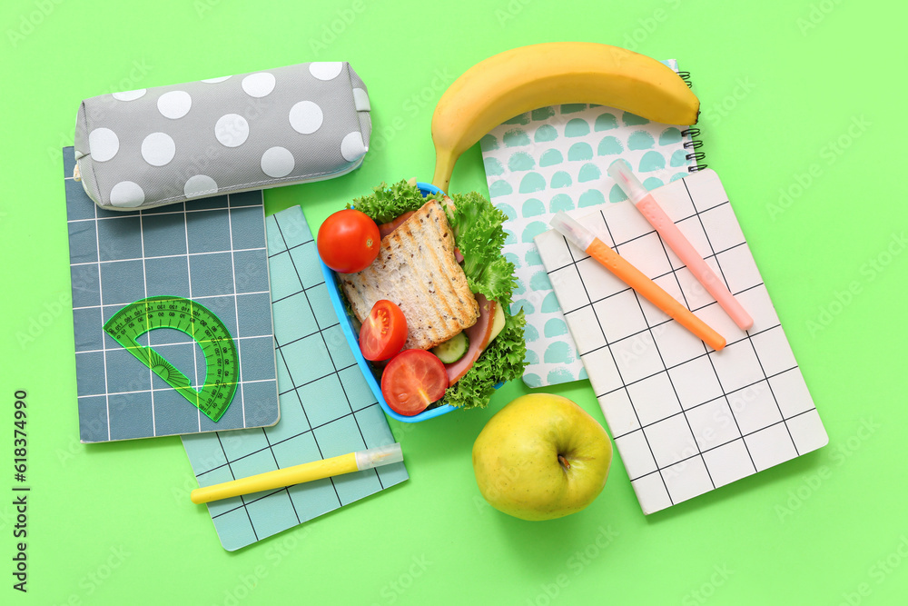 Different stationery and lunch box with tasty food on green background