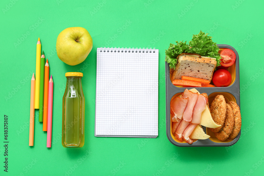 Stationery, blank notebook, drink and lunch box with tasty food on green background