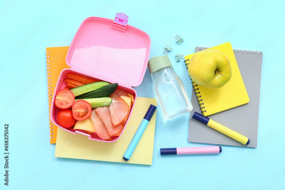 Stationery, drink and lunch box with tasty food on blue background