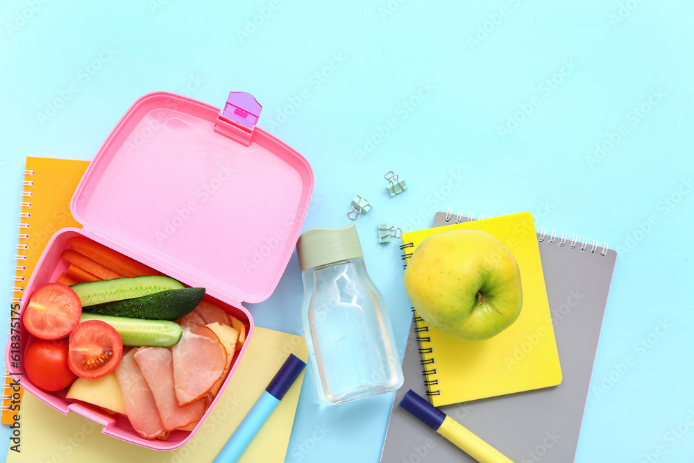 Stationery, drink and lunch box with tasty food on blue background