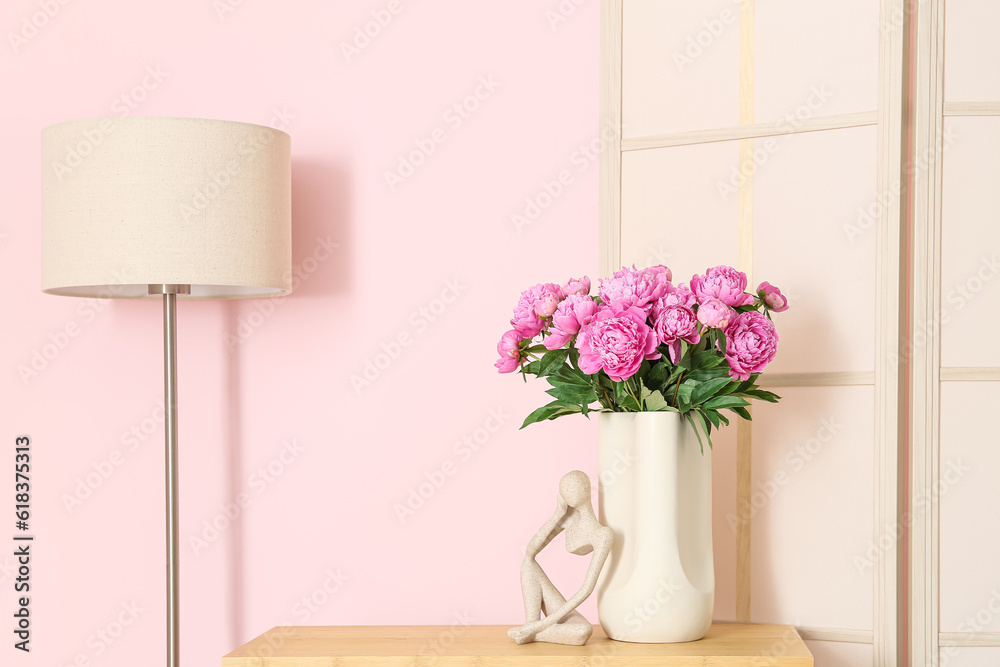 Vase of pink peonies on shelving unit, dressing screen and floor lamp near color wall