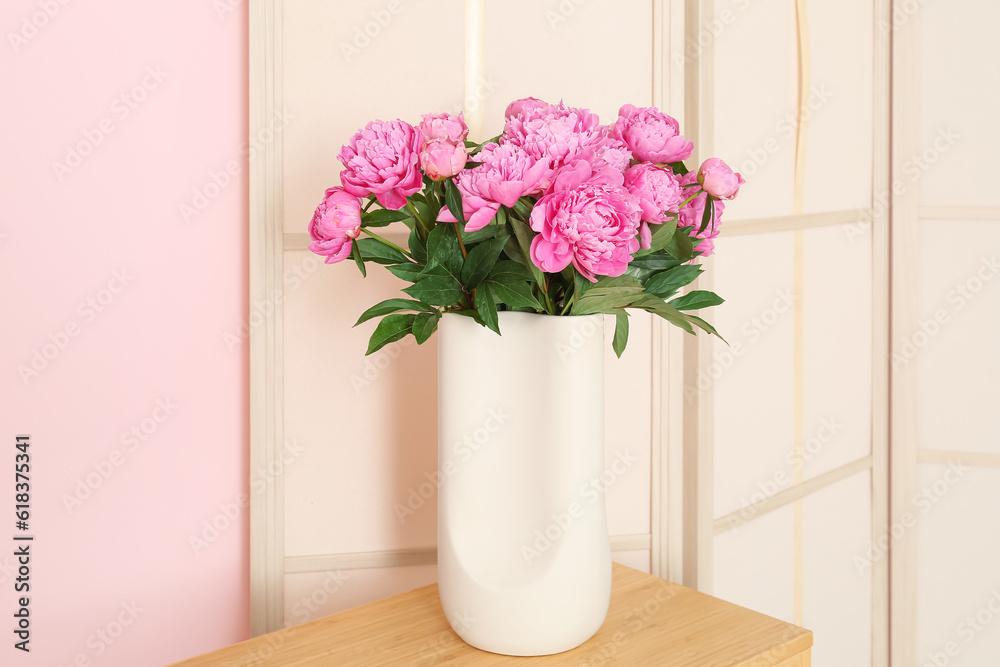 Vase of pink peonies on shelving unit with dressing screen near color wall